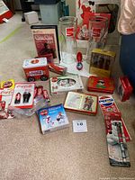 Full view of Coca-Cola collectibles including playing cards, tin boxes, lighters, pens, and glasses arranged on the floor