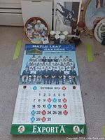 Photo showing 1973 Maple Leafs calendar, hockey collector plate box, and bobblehead with other memorabilia on carpeted floor