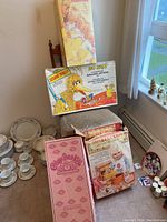 Overall view of items including boxed Thumbelina doll, Sesame Street Walking Letters set, Jello pudding set, and boxed Cabbage Patch Kids doll along with tea set in background