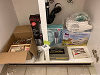 Under-sink cabinet containing all lot items including the nebulizer, curling iron, style shaper, thermometer, and vintage curlers in boxes