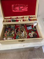 Wooden jewelry box open showing top and bottom compartments filled with assorted jewelry including necklaces at center and loose pieces.