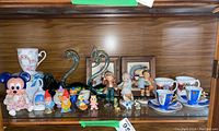 Wide shelf view showing Disney figurines, garden gnomes, decorative cups, and glass swan sculptures.