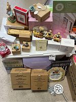 Overview photo showing large assortment of holiday and home decor items including boxed suncatchers, figurines, and plaques on a table.