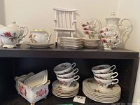 Full tea set displayed on shelf showing teapot, sugar bowl, cream pitcher, cups, saucers, dessert plates, and additional china items.