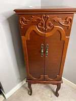 Front view of the closed jewelry armoire cabinet showing carved wood design and metal handles.