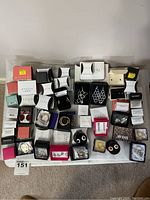 Top view of large assortment of Avon earrings in variously colored branded boxes laid out on white surface, showing multiple pairs inside and outside of packaging.