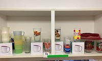 Full shelf with assortment of mugs and promotional glasses, showing variety of brands and styles including Asobu mugs in box, pastel mugs, and multiple branded glasses
