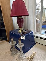 Burgundy lamp with shade, extension cord, two clear glass lamp bases, magnet sitting on blue tote with window background.
