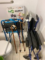 Photo showing lightweight blue foldable transfer wheelchair with black fabric seat, blue Hugo Walker frame in box, and several canes.