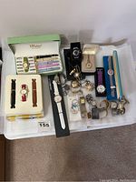 Full lot showing collection of new and used watches, including boxed set with multiple bands and various wristwatches and pocket watches arranged on a white fabric surface.