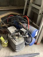 Overview of Campbell Hausfeld air compressor unit with blue tank and motor, with numerous hoses and tools coiled over it, resting on concrete floor.