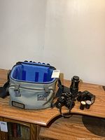 Wide photo showing the camera body, lenses, flash, film rolls, and carrying bag on wooden surface.
