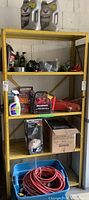 Overall view of yellow shelving with motor oil jugs, small fluid bottles, wax kit, adapter, power pack, jack, vacuum box and tote below