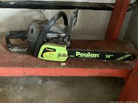 Side view of entire chainsaw on metal shelf, showing housing, handle and guide bar