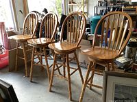 Four solid wood swivel counter stools lined up indoors in a garage area.