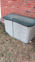 Outdoor Rubbermaid deck storage box with dark green lid and gray body, closed showing front and top view