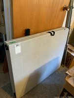 Full view of the folded plastic table standing upright, showing overall shape and condition