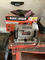 Shopcraft bench grinder with visible grinding wheels, power cord, and protective shields, placed on a wooden bench with visible wear.