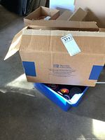Two cardboard boxes and a blue plastic tote containing multiple hockey pucks