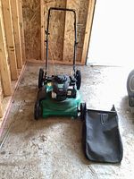 Full frontal view of the Weed Eater push lawnmower with mulch bag next to it on the floor.