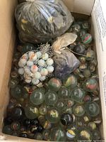 Box with assorted glass marbles of various sizes and color swirls, some loose and some in plastic bags and mesh netting.