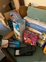 Overview photo showing Dr. Ho's Circulation Promoter, Muscle Therapy device, foot massager sandals, and part of Conair spa pillow in background.