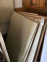 Stack of beige peg boards with perforated holes leaning against wall in garage.