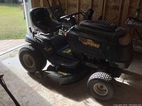 Front and side view of green Yard Works riding mower parked inside a garage; shows hood, seat, deck and tires