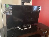 Full frontal view of the Seiki flat-screen TV on its stand with the remote in a plastic bag taped to the side.