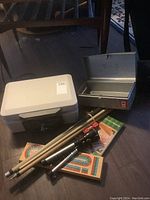 Photo showing closed SentrySafe 1100 lockbox, cribbage board, three pool cues, and folded tripod light base.