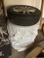 Four tires stacked and wrapped in white plastic stored in a garage area.