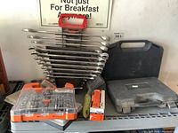 Shelf with wrench set on red rack, socket set in orange plastic case, finishing nails box, and utility brush
