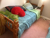 Full view of twin pine bed with blue bedding, pillows, red heart pillow and green crocodile plush.