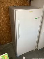 Front angled view showing white Frigidaire upright freezer against particle board wall with vertical handle.