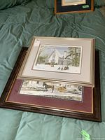 Photo of two framed prints stacked on bed, showing overall presentation and relative size.
