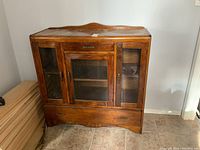 Front view of wood china cabinet showing three glass doors with wooden frames and lower drawer.