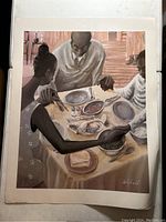 Photo of the framed print depicting a family holding hands in prayer before a meal, showing the full image with clear view of the artwork and signature.