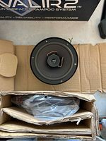 Top view of one small round speaker on cardboard packaging showing cone and tweeter with copper wiring.