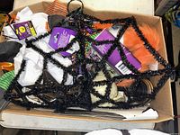 Box containing various Halloween decorations such as a black and orange tinsel spider web, fabric pieces in orange, white, and black, with some plastic bat shapes and other items.
