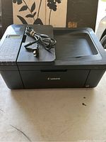 Front angled view of black Canon Pixma printer with power cord coiled and placed on top.