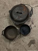 Top view of 3 Lodge cast iron pots showing large Dutch oven with lid, medium pot, and small pot on concrete floor.
