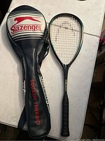 Slazenger squash racquet with its black, red and white protective case laid side by side on a white surface.