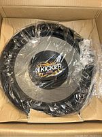 Kicker CVR speaker tightly wrapped in clear plastic inside a cardboard box showing the speaker cone and logo.