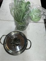 Top view of green kitchen utensils in holder and stainless steel pot with lid