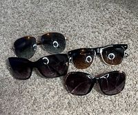 Four pairs of sunglasses displayed on carpet showing various styles and lens colors, visible lenses and frames with scratches and wear.