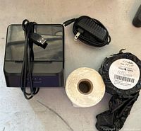 Milestone label printer with USB cable on top, power adapter, and two rolls of labels next to it on a white surface.