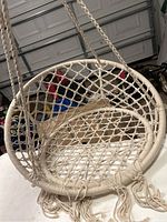 Beige hanging hammock chair, close-up image showing woven net design and hanging ropes in a garage setting