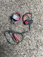 PowerBeats wireless earphones laid on carpet showing both earbuds, ear hooks, and inline remote control.