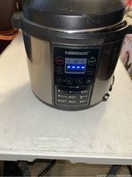 Front view of Farberware digital pressure cooker powered on, display lit, placed on white table.