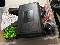 Photo showing black Plano tackle box, green rod holders, white triangular pieces, Bicycle playing cards in packaging.